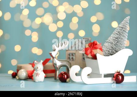Traîneau blanc avec boîtes cadeaux et décoration de Noël sur table bleu clair avec lumières floues Banque D'Images