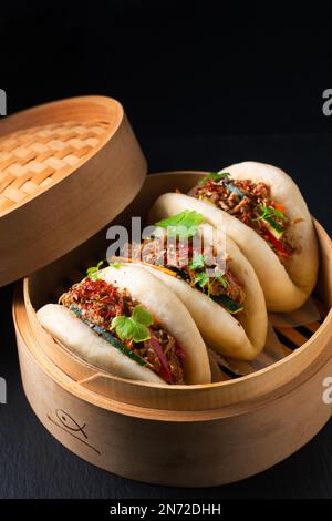 Concept alimentaire Buns Bao de bœuf bio ou Gua Bao dans plateau de ruisseau de bambou sur fond noir avec espace de copie Banque D'Images