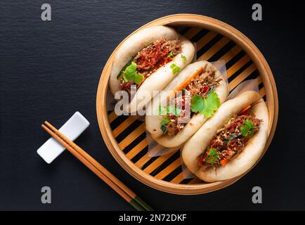 Concept alimentaire Buns Bao de bœuf bio ou Gua Bao dans plateau de ruisseau de bambou sur fond noir avec espace de copie Banque D'Images