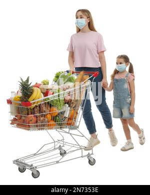 Mère et fille dans des masques médicaux avec chariot plein de provisions sur fond blanc Banque D'Images