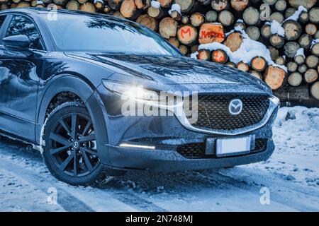 Italie, Vénétie, Belluno, une Mazda Motor Corp Véhicule utilitaire sport (vus) multisegment CX-30 en hiver, stationné près d'une pile de billes de sapin dans les Dolomites Banque D'Images