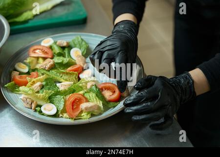 Le chef féminin en gants de protection décore une assiette de salade Banque D'Images