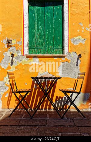 Deux chaises en bois et une table devant un mur de maison avec du plâtre qui s'écaille Banque D'Images