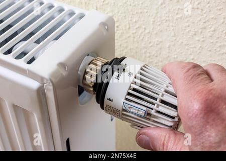 Main masculine réduit la température de la pièce sur le thermostat du radiateur, le réglage de l'icône des flocons de neige, la protection contre le gel environ ö°C., l'image de l'icône, les coûts d'énergie, la hausse des coûts de chauffage, Banque D'Images