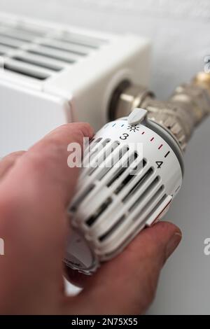 La main de l'homme tourne un thermostat de radiateur, niveau de réglage 3 env. 2ö°C., image de symbole, coûts énergétiques, Banque D'Images