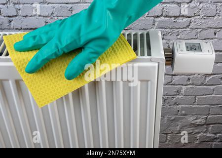 Nettoyer le radiateur avec une éponge extérieure, un fond blanc mur brique, image symbole, nettoyer régulièrement, améliore les performances de chauffage, Banque D'Images