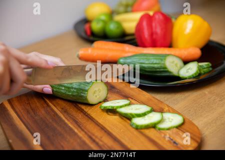 les mains des femmes trancheuses un concombre sur une planche à découper en bois Banque D'Images