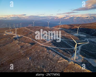 Moulins à vent sur les collines pendant le coucher du soleil. Énergies renouvelables, énergies vertes. Montagnes en arrière-plan avec de la neige. Énergie éolienne et écologique. Banque D'Images