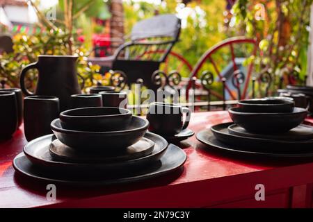 Un ensemble de repas peint en noir repose sur une table rouge à l'extérieur, avec une végétation verte servant de toile de fond. Banque D'Images