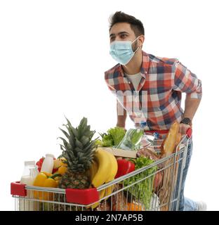 Jeune homme dans un masque médical avec un chariot plein de provisions sur fond blanc Banque D'Images