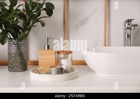 Vase avec branches vertes, distributeur de savon et tampons de coton près de l'évier de bateau dans la salle de bains Banque D'Images