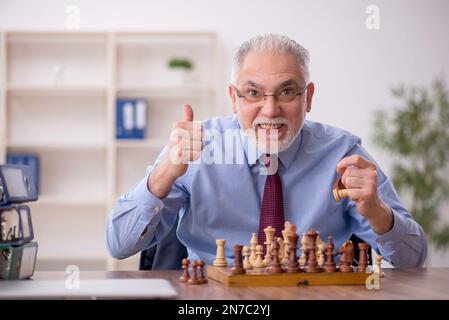 Un vieil employé de sexe masculin joue aux échecs dans le bureau Banque D'Images