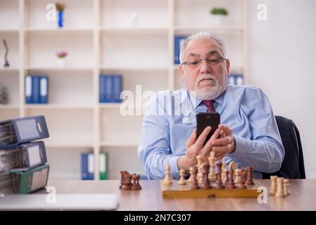 Un vieil employé de sexe masculin joue aux échecs dans le bureau Banque D'Images