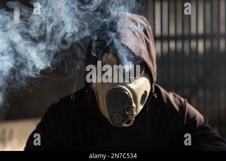 Un homme dans un masque à gaz tenant une bombe de fumée. Rouge vif fumée colorée. Ancien masque à gaz tchécoslovaque M-10(M). Banque D'Images