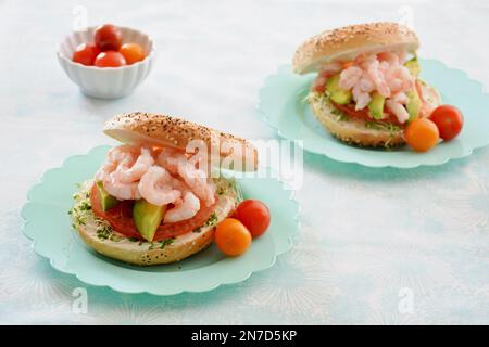 Crevettes fraîches et savoureuses au fromage à la crème, à l'avocat, à la tomate et aux pousses sur le bagel aux graines. Sur de jolies assiettes turquoise festonnées au format horizontal. Hé Banque D'Images