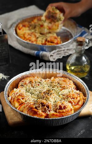 Pizza au fromage à emporter. Servi sur une plaque de cuisson feuille d'aluminium, avec une tranche à l'arrière-plan prise à la main Banque D'Images