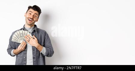 Un homme souriant qui fait de l'argent, enserre des billets de dollars avec un visage soulagé heureux, debout sur fond blanc Banque D'Images