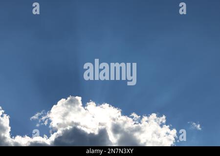 Nuages avec des rayons de lumière qui sortent d'eux contre un ciel bleu vif Banque D'Images