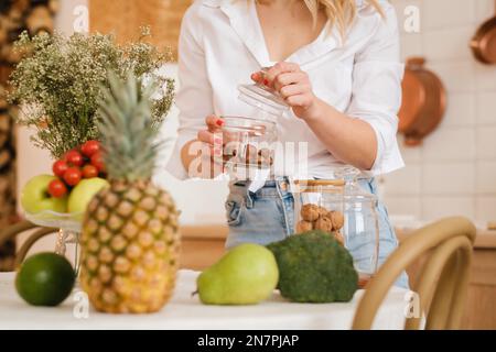gros plan des mains de l'hôtesse tenant des noix dans un pot et des légumes couchés, des fruits au premier plan sur la table de cuisine. cuisson. Banque D'Images