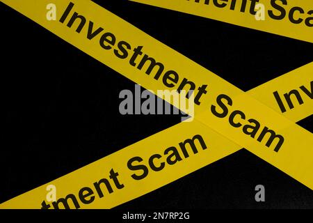 Escroquerie d'investissement et alerte à la fraude, mise en garde et avertissement. Ruban de barricade jaune avec mot sur fond noir foncé. Banque D'Images