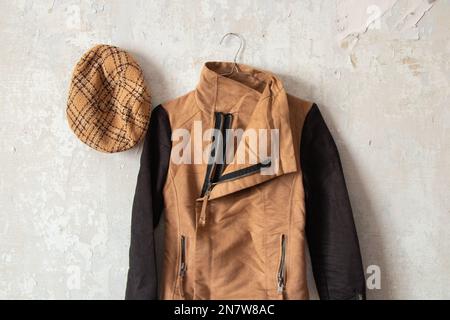 une veste marron pour femmes et une casquette à carreaux sont accrochées sur un mur blanc à la maison Banque D'Images