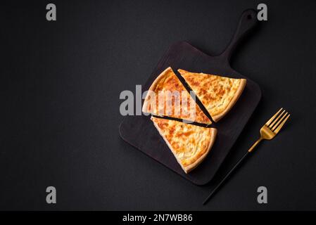 Belle tarte délicieuse à la quiche avec quatre types de fromage aux épices et aux herbes sur fond de béton foncé Banque D'Images