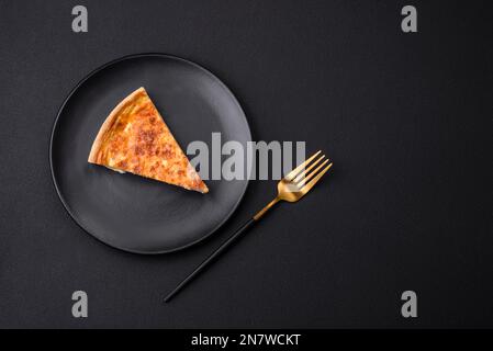 Belle tarte délicieuse à la quiche avec quatre types de fromage aux épices et aux herbes sur fond de béton foncé Banque D'Images