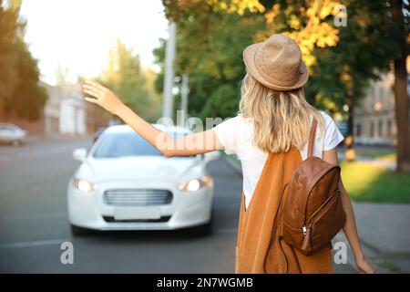 Jeune femme prenant un taxi dans la rue de la ville, vue arrière Banque D'Images