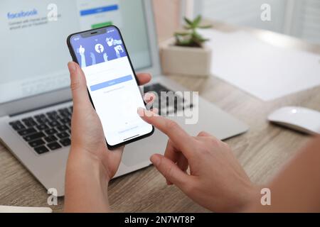 MYKOLAIV, UKRAINE - 28 AOÛT 2020: Femme tenant l'iPhone 11 avec l'application Facebook à l'écran à table, gros plan Banque D'Images