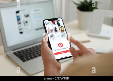 MYKOLAIV, UKRAINE - 28 AOÛT 2020: Femme tenant l'iPhone 11 avec l'application Pinterest à l'écran à la table, gros plan Banque D'Images