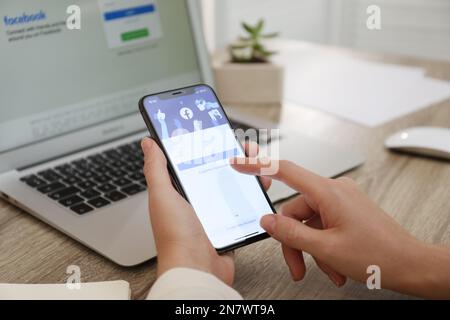 MYKOLAIV, UKRAINE - 28 AOÛT 2020: Femme tenant l'iPhone 11 avec l'application Facebook à l'écran à table, gros plan Banque D'Images