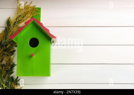 Belle maison d'oiseaux verte et fleurs mimosa sur fond blanc en bois, plat. Composition de ressort avec espace pour le texte Banque D'Images