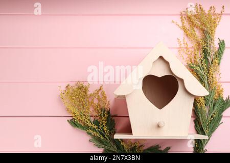 Belle maison d'oiseaux avec trou en forme de coeur et fleurs mimosa sur fond de bois rose, espace pour le texte. Composition de la pose à plat à ressort Banque D'Images