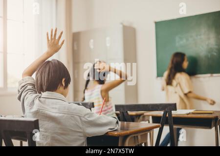 éducation des enfants dans la salle de classe. garçon lève la main pour demander le problème d'enseignant Banque D'Images