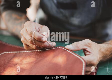 gros plan le travail à la main le cuir la main dans l'atelier de cuir. Homme tenant un outil de fabrication et travaillant. Il est marteau à coudre pour faire une morette. Ta Banque D'Images