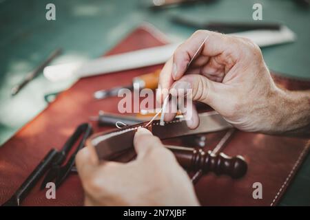 gros plan le travail à la main le cuir la main dans l'atelier de cuir. Homme tenant un outil de fabrication et travaillant. Il est marteau à coudre pour faire une morette. Ta Banque D'Images