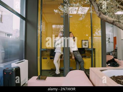 Deux collègues masculins et féminins attrayants ayant un appel téléphonique dans les cabines téléphoniques au bureau Banque D'Images