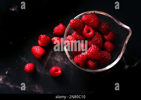 Une portion de framboises dans un petit bol transparent sur une surface en granit noir. Aliments sombres, orientation horizontale, espace pour le texte. Banque D'Images