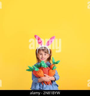 Bonne petite fille avec des oreilles de lapin et une poignée de carottes sur fond orange. Fête de Pâques Banque D'Images