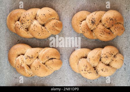 Quatre petits pains tressés au four, faits de farine d'épeautre de grain entier, saupoudrées de graines de pavot Banque D'Images