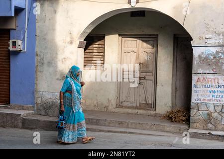 DIU, Inde - décembre 2018 : une femme indienne portant un sari bleu vif marchant devant une porte arquée vintage dans la ville de l'île de DIU. Banque D'Images