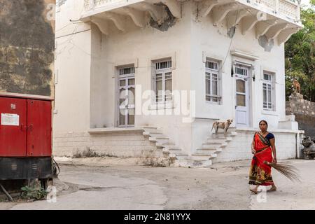 DIU, Inde - décembre 2018 : une femme indienne portant un sari rouge marchant avec un bâton de balai devant une ancienne maison de l'époque portugaise dans la ville de l'île de DIU. Banque D'Images