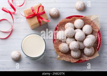 Biscuits maison de Noël au pain d'épice saupoudrés de sucre en poudre sur une assiette rouge sur fond bleu clair avec cadeau enveloppé dans du papier artisanal avec du rouge R. Banque D'Images