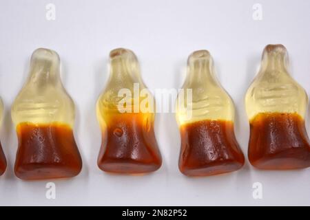 La mastication lumineuse pour enfants, les bonbons en gelée sous forme de boissons, les bouteilles de cola sont situées sur un fond blanc. Banque D'Images