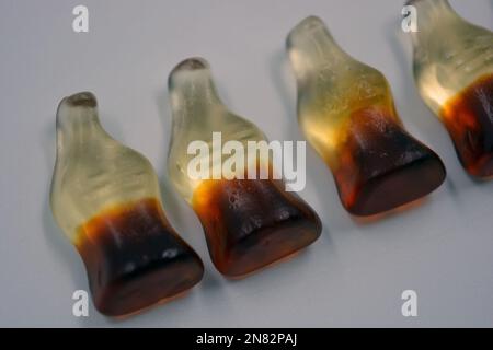 La mastication lumineuse pour enfants, les bonbons en gelée sous forme de boissons, les bouteilles de cola sont situées sur un fond blanc. Banque D'Images