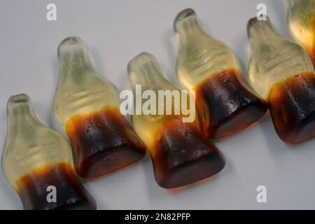 La mastication lumineuse pour enfants, les bonbons en gelée sous forme de boissons, les bouteilles de cola sont situées sur un fond blanc. Banque D'Images