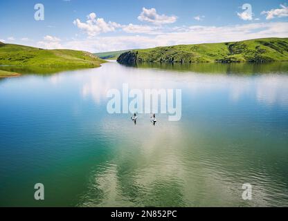 Haut vers le bas tir de drone aérien de deux hommes à stand up paddle boards SUP dans le lac de montagne près des collines vertes au Kazakhstan Asie centrale Banque D'Images