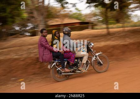 Caratu, Tanzanie - 16 octobre 2022: Trois personnes qui font une moto sur une route de terre en Tanzanie. Banque D'Images