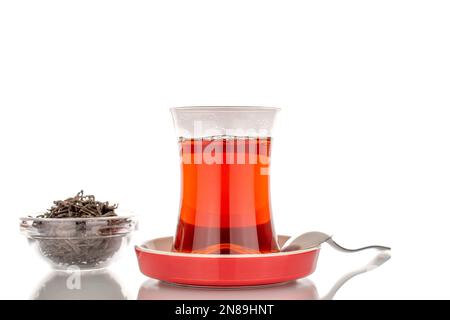 Un verre de thé aromatique noir avec une cuillère en métal sur une soucoupe en céramique, macro, isolée sur fond blanc. Banque D'Images