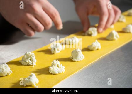 Jeune homme Chef de la fabrication des raviolis. Plats italiens raviolis de pâtes maison sur fond métallique. Banque D'Images